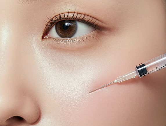 눈 밑 볼에 주사 바늘이 닿은 얼굴 클로즈업